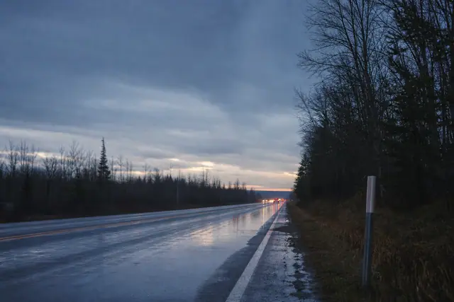 A wet Ontario highway at dusk, with oncoming headlights reflected on the road surface.